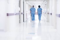 Dos doctores vistiendo bata quirúrgica caminando en el pasillo, vista trasera . - foto de stock