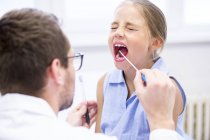 Arzt entnimmt Abstrichprobe aus Mund eines jungen Mädchens. — Stockfoto