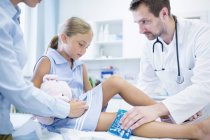 Arzt legt Eisbeutel auf Bein eines jungen Mädchens. — Stockfoto