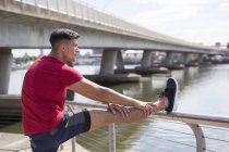 Mann streckt Bein auf Geländer am Flussufer. — Stockfoto