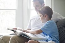 Son reading book with father on sofa. — Stock Photo