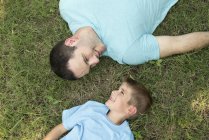 Vater und Sohn liegen im Gras, Blick über den Kopf. — Stockfoto