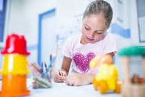 Девушка сидит с цветными карандашами за столом . — стоковое фото