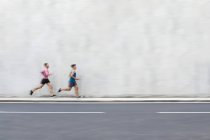 Atletas do sexo masculino correndo na rua em frente à parede de concreto — Fotografia de Stock