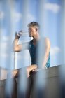 Человек, сидящий на крыше и пьющий воду из бутылки, за забором — стоковое фото
