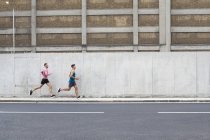 Male athletes running on street in front of building — Stock Photo