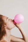 Profile of young woman with red hair blowing up pink balloon. — Stock Photo