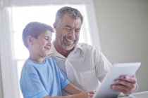 Avô e neto usando tablet digital e sorrindo dentro de casa . — Fotografia de Stock