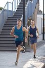 Male athletes running on street past steps. — Stock Photo