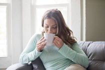 Young woman drinking hot drink from mug. — Stock Photo