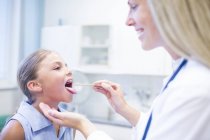 Mujer médico examinando joven chica lengua . - foto de stock