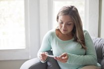 Woman sitting on sofa and looking down at pregnancy test. — Stock Photo