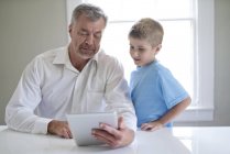 Grand-père et petit-fils utilisant une tablette numérique à l'intérieur . — Photo de stock