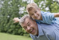 Abuelo llevando a su nieto en hombros con los brazos hacia fuera, retrato . - foto de stock