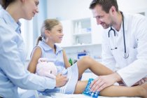 Homme médecin mettre glace pack sur jeune fille jambe . — Photo de stock