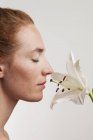 Woman with eyes closed smelling white flower, side view. — Stock Photo
