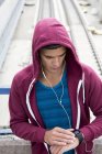 Man wearing earphones and hooded top checking sports watch. — Stock Photo