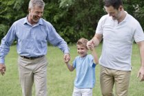 Grandfather, father and boy holding hands and smiling outdoors. — Stock Photo