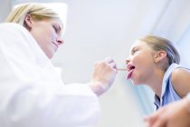 Médico feminino examinando jovem língua menina . — Fotografia de Stock