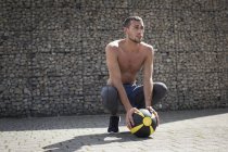 Man crouching with medicine ball in front of stone wall. — Stock Photo