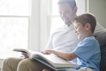 Син читає книгу з батьком на дивані . — стокове фото