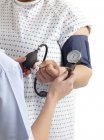 Обрізаний вид лікаря, який приймає кров'яний тиск пацієнта в лікарняній сукні . — стокове фото