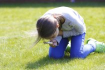 Girl examining grass with magnifying glass in garden. — Stock Photo