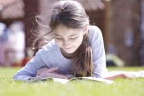 Preteen girl lying on blanket on green meadow in garden and reading book. — Stock Photo