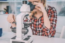 Female biology student using light microscope in laboratory. — Stock Photo