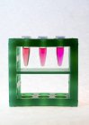 Tres tubos microcentrifugadores con líquido rosa en el estante del tubo . - foto de stock