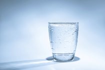 Склянка води з конденсатом на звичайному фоні . — стокове фото