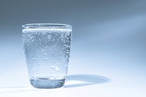 Glass of water with condensation on plain background. — Stock Photo