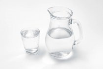 Bicchiere e brocca con acqua potabile su fondo bianco . — Foto stock