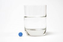 Синя таблетка і склянка води на білому тлі . — стокове фото