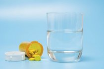 Medication and glass of water on blue background. — Stock Photo
