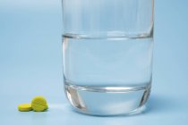 Pills and glass of water on blue background. — Stock Photo