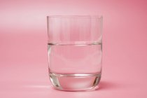 Glass of clean water on pink background. — Stock Photo