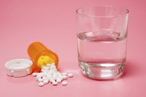 Medicamentos y vaso de agua sobre fondo rosa
. - foto de stock