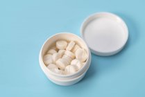 Weiße Tabletten in einem Plastikbehälter auf blauem Hintergrund. — Stockfoto