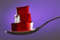 Cubes of red jelly on spoon on purple background. — Stock Photo