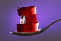 Cubes of red jelly on spoon on purple background. — Stock Photo