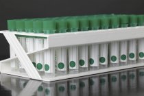 Tubos de ensayo de plástico con tapas verdes en rack . - foto de stock