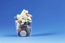 Verschiedene Pillen im Plastikbecher auf blauem Hintergrund. — Stockfoto