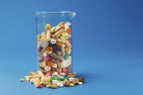 Glass flask with colorful pills of various shapes on blue background. — Stock Photo