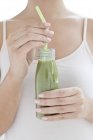 Cropped view of woman drinking green smoothie from bottle. — Stock Photo