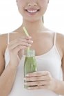 Young smiling woman drinking green smoothie. — Stock Photo
