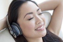 Mujer asiática escuchando música en auriculares con los ojos cerrados . - foto de stock