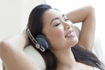 Mulher em poltrona usando fones de ouvido e ouvindo música com os olhos fechados . — Fotografia de Stock