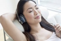 Mulher em poltrona usando fones de ouvido e ouvindo música com os olhos fechados . — Fotografia de Stock