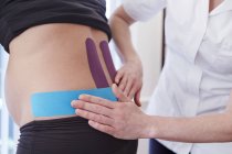 Osteopath klebt Klebeband an schwangere Patientin, abgeschnittene Ansicht. — Stockfoto